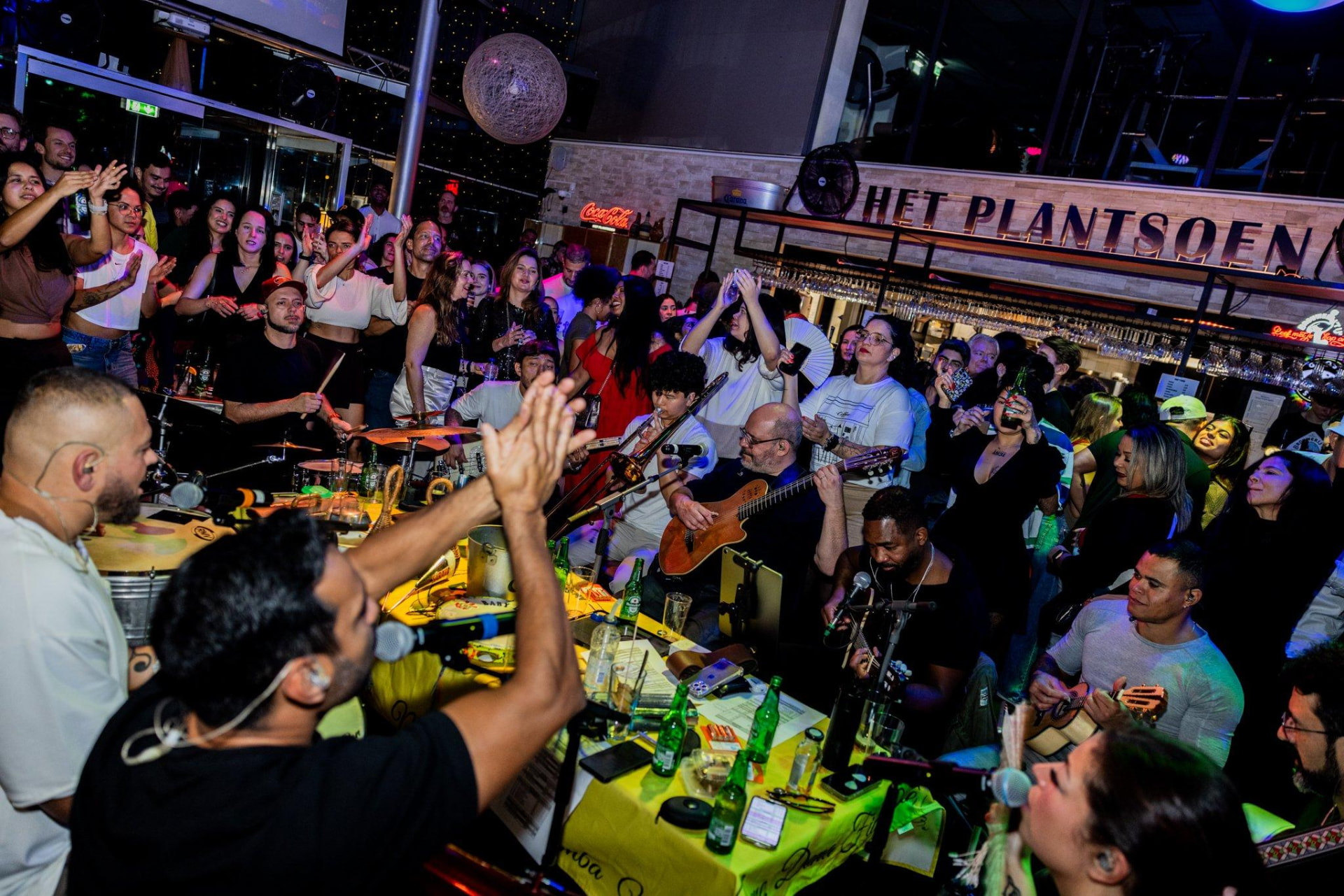 Druk feest met live band in Het Plantsoen, met het Plantsoen-logo op de achtergrond
