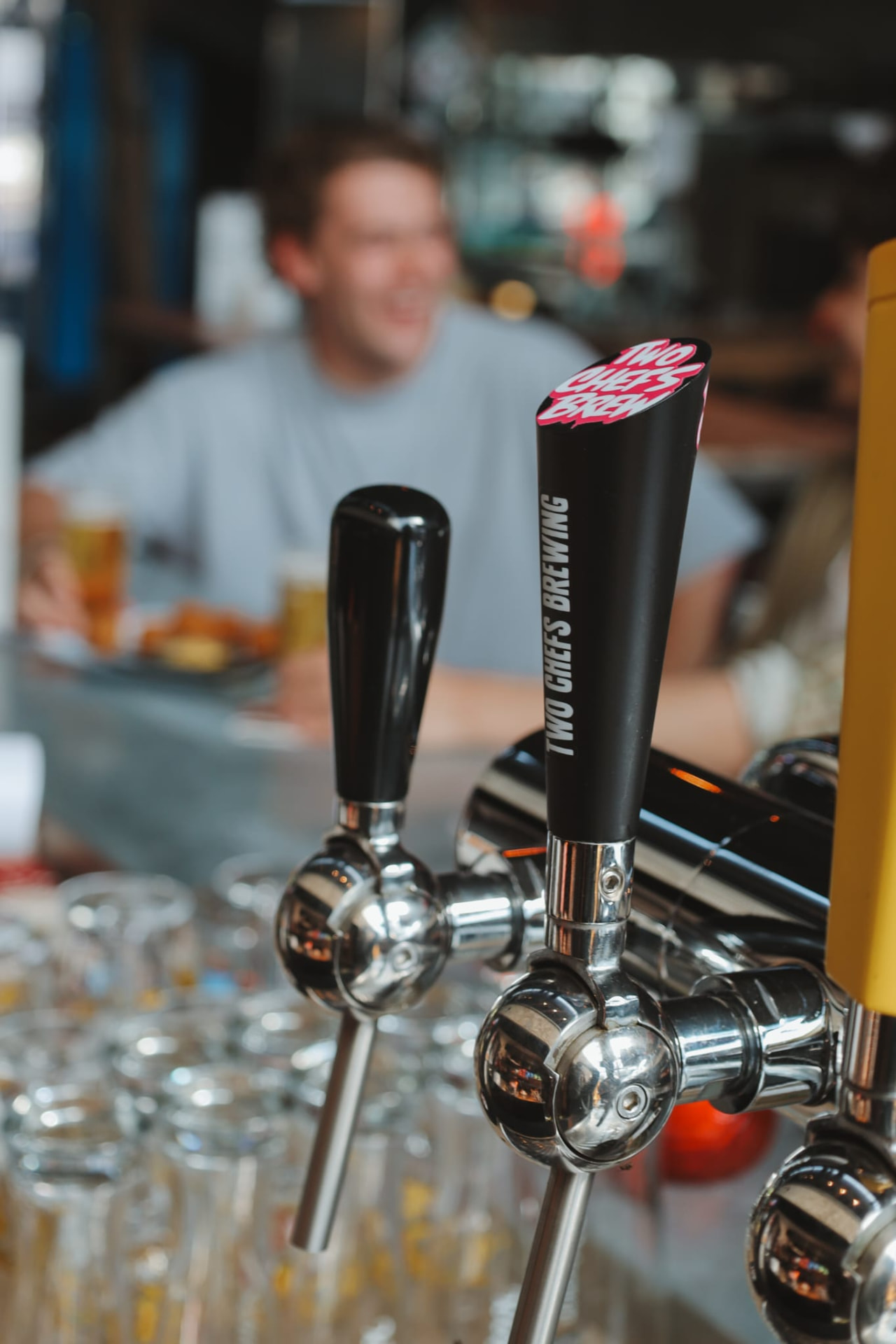 Biertaps aan de bar met een lachende gast op de achtergrond