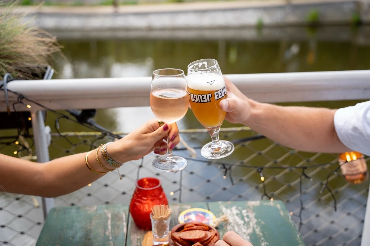 Twee mensen toosten met een glas bier aan het water bij Het Plantsoen