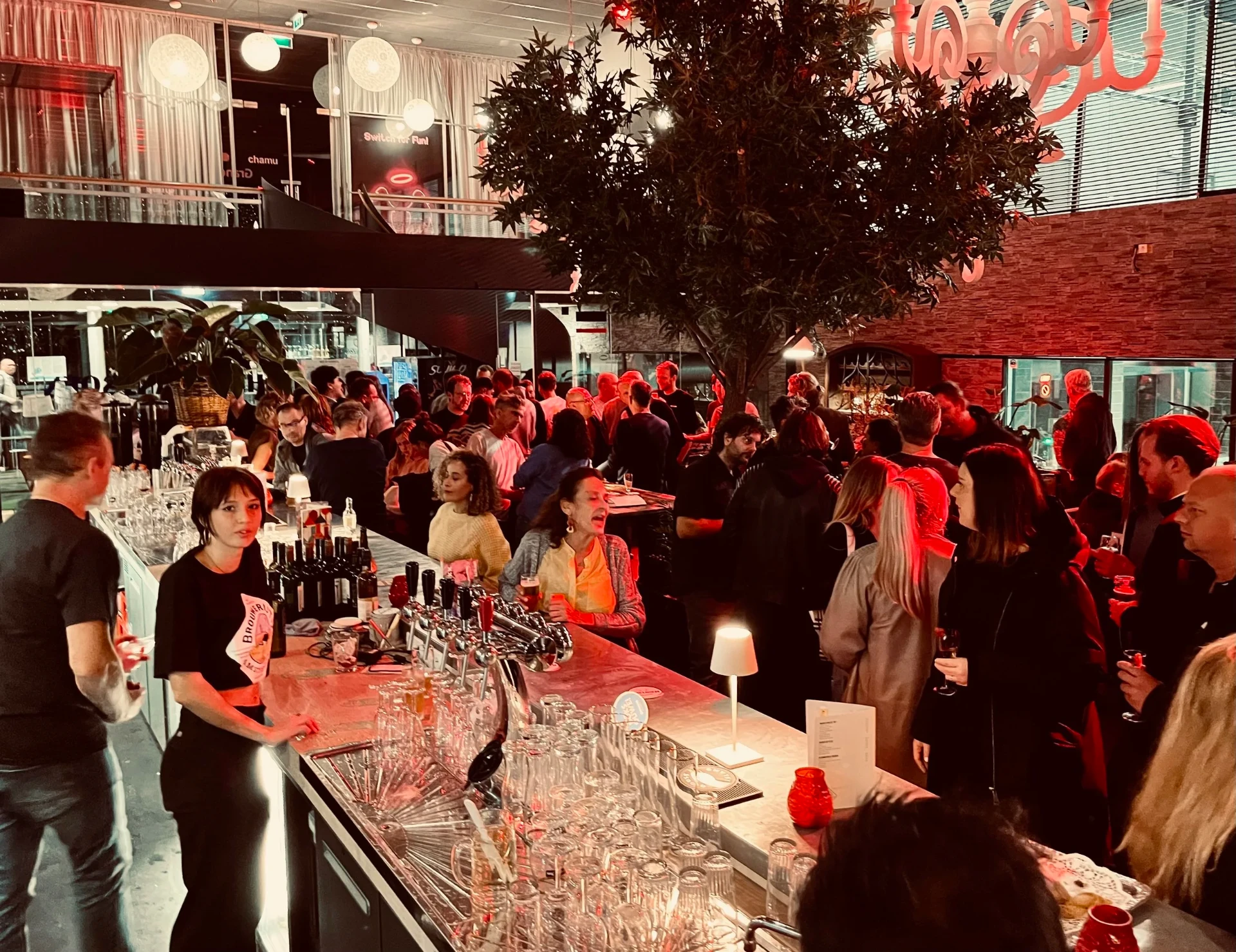 Drukke avond met gasten aan de lange bar onder de grote boom in Het Plantsoen